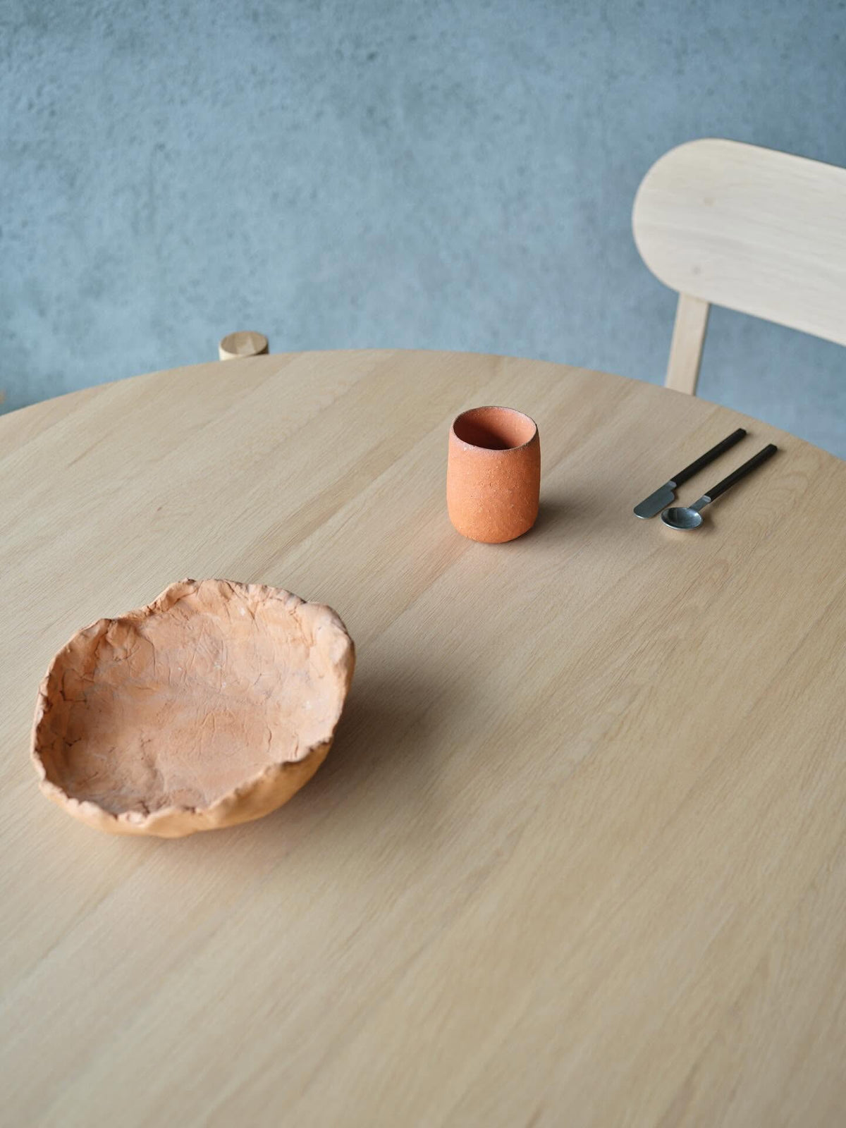 Table ronde Castor 110 — plateau en chêne vu de dessus, avec coupe en bois et tasse terracotta | Antifer