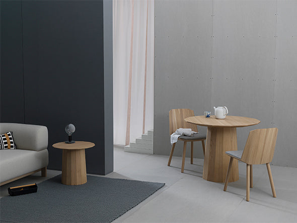 Chaise Colour Wood et table ronde dans une scénographie claire, devant une cloison sombre | Antifer