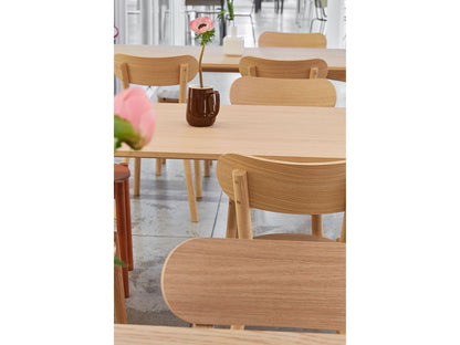 Chaises Castor en chêne, cadrage serré sur une table de showroom fleurie | Antifer