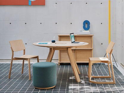 Table ronde Spectrum ST 120 en chêne dans un espace de travail en béton, avec chaises Colour Wood et pouf — Karimoku New Standard | Antifer