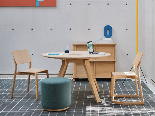 Table ronde Spectrum ST 120 en chêne dans un espace de travail en béton, avec chaises Colour Wood et pouf — Karimoku New Standard | Antifer