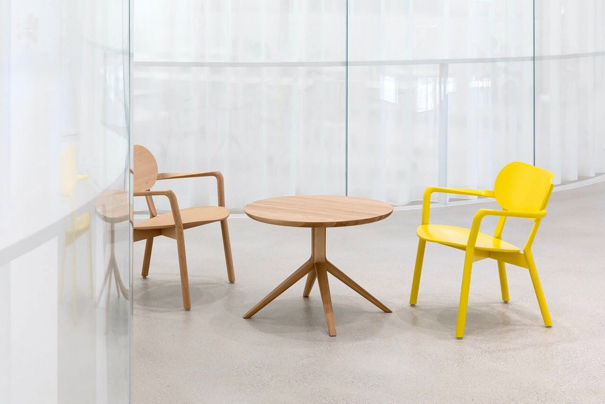 Table bistrot Scout en chêne entre deux fauteuils Castor, l'un en chêne et l'autre jaune, derrière un voilage | Antifer