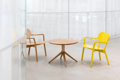 Table bistrot Scout en chêne entre deux fauteuils Castor, l'un en chêne et l'autre jaune, derrière un voilage | Antifer