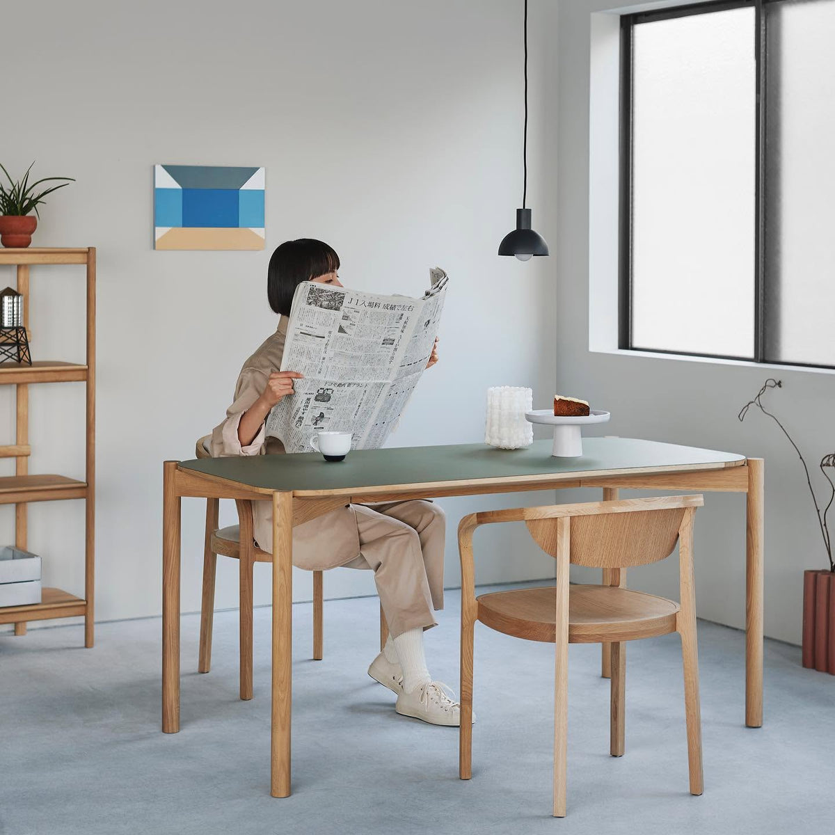 Table Castor 180 à plateau linoléum vert dans un intérieur clair, une femme y lit le journal | Antifer