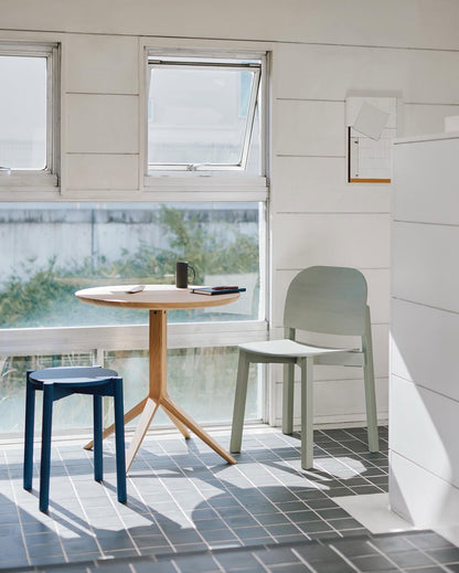 Table bistrot Scout en chêne devant une fenêtre, avec tabouret Castor bleu et chaise Chesa verte | Antifer
