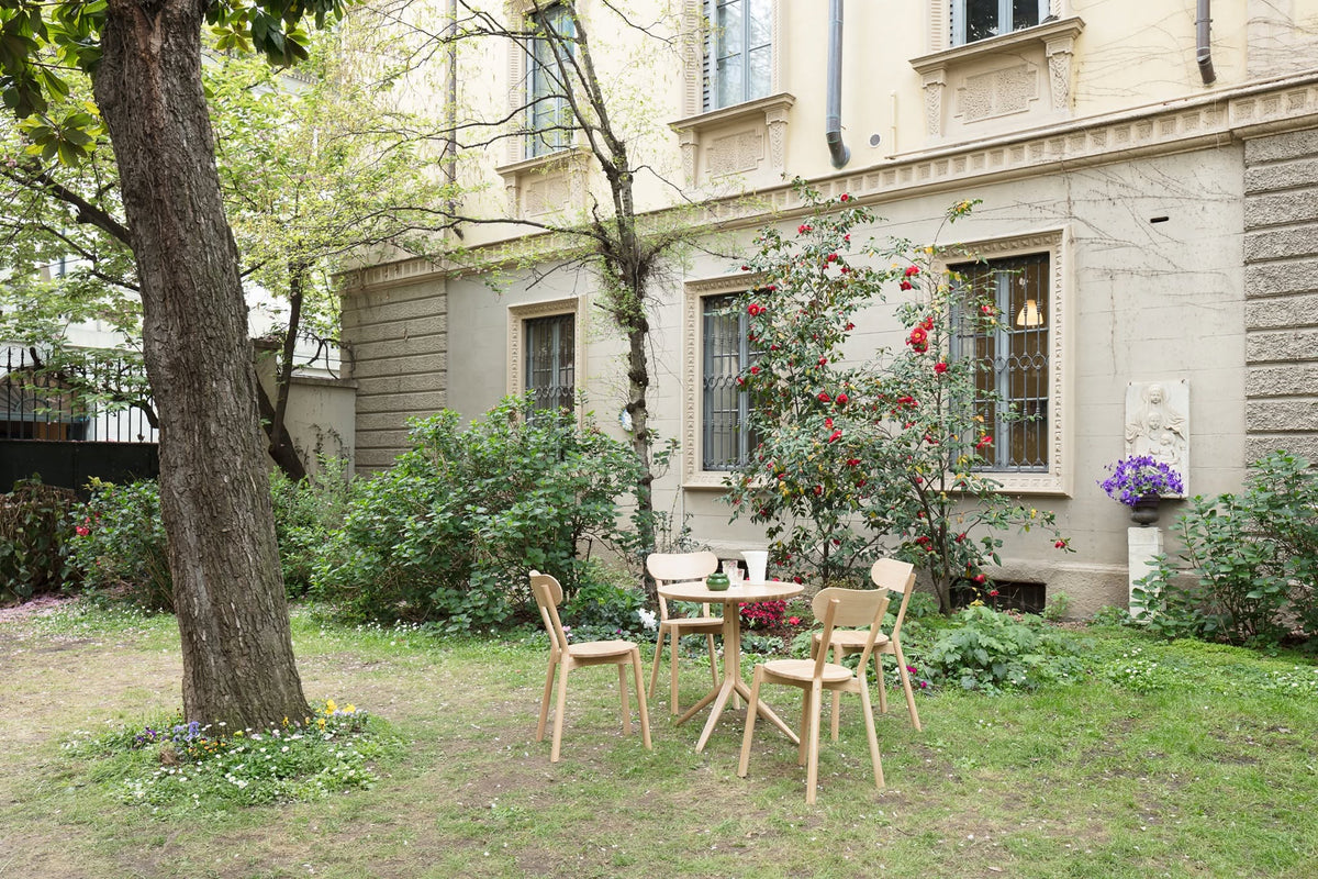 Table bistrot Scout et deux chaises dans un jardin, devant la façade d'un immeuble ancien | Antifer