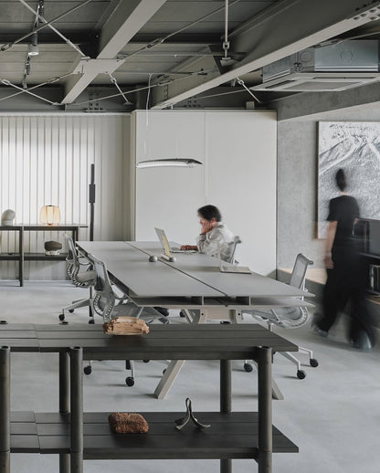 Bureaux Spectrum noirs alignés sur un plateau en béton, sous une suspension ovale — Karimoku New Standard | Antifer