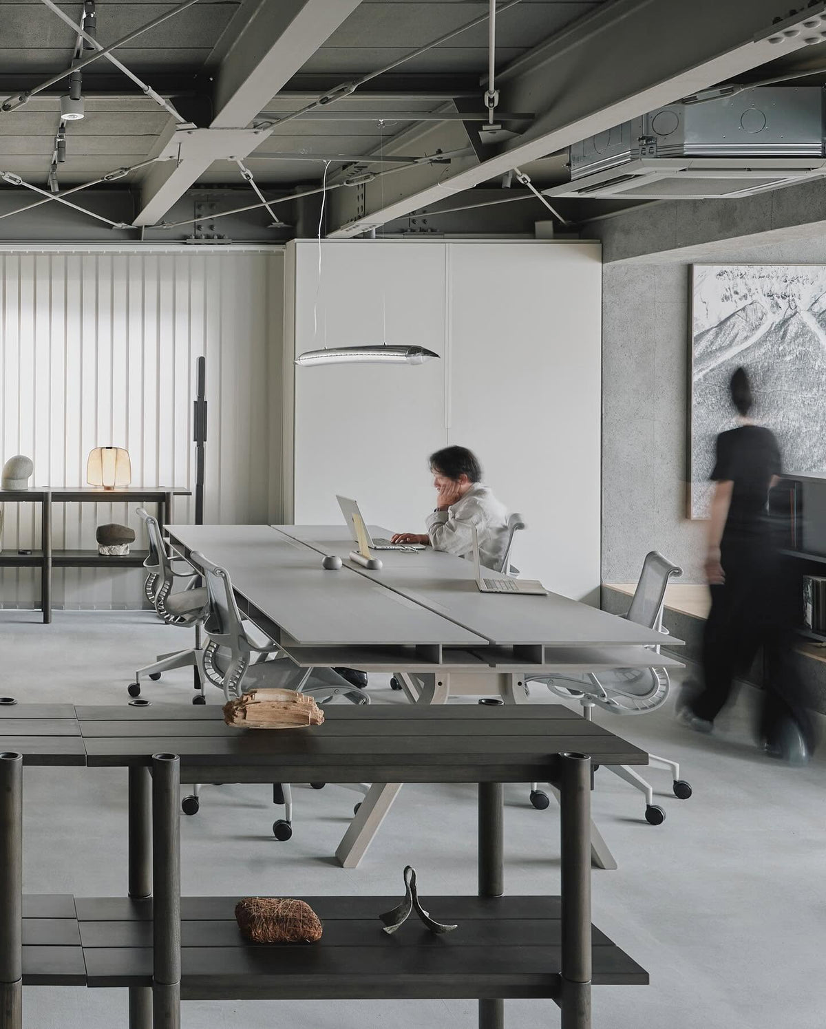 Bureaux Spectrum noirs alignés sur un plateau en béton, sous une suspension ovale — Karimoku New Standard | Antifer